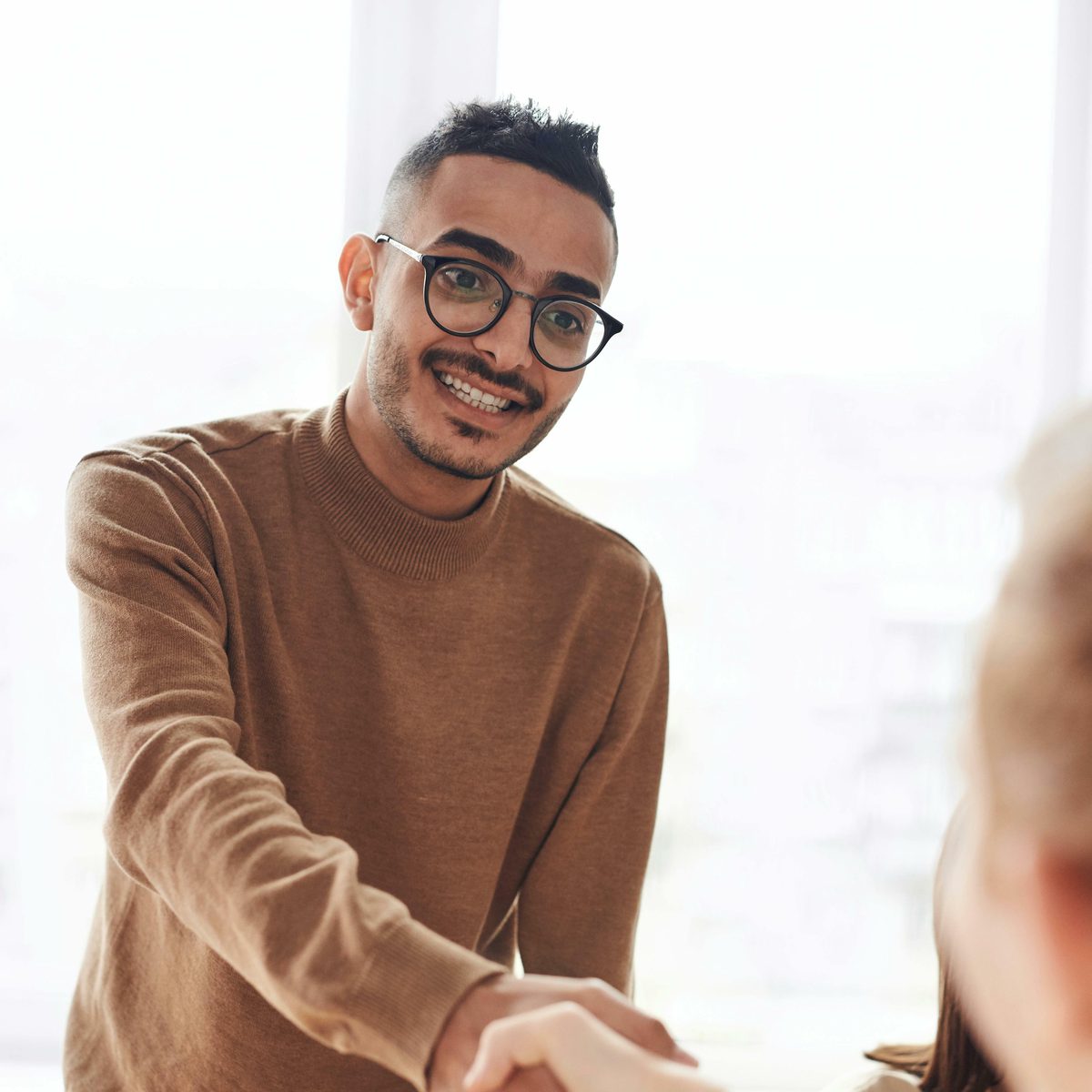 Young person standing at table shacking the hand of a seated person across from them.